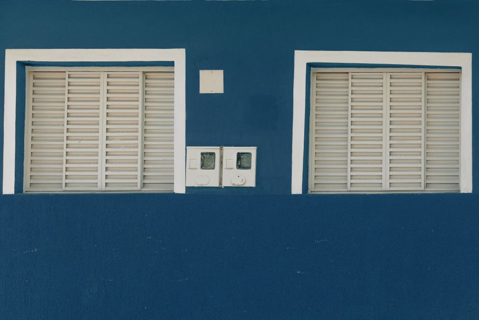 A blue painted wall with two white shuttered windows