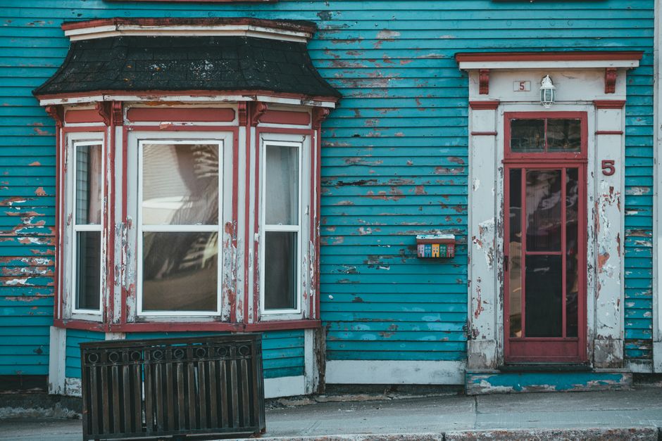 An aged blue painted wall with a window and door