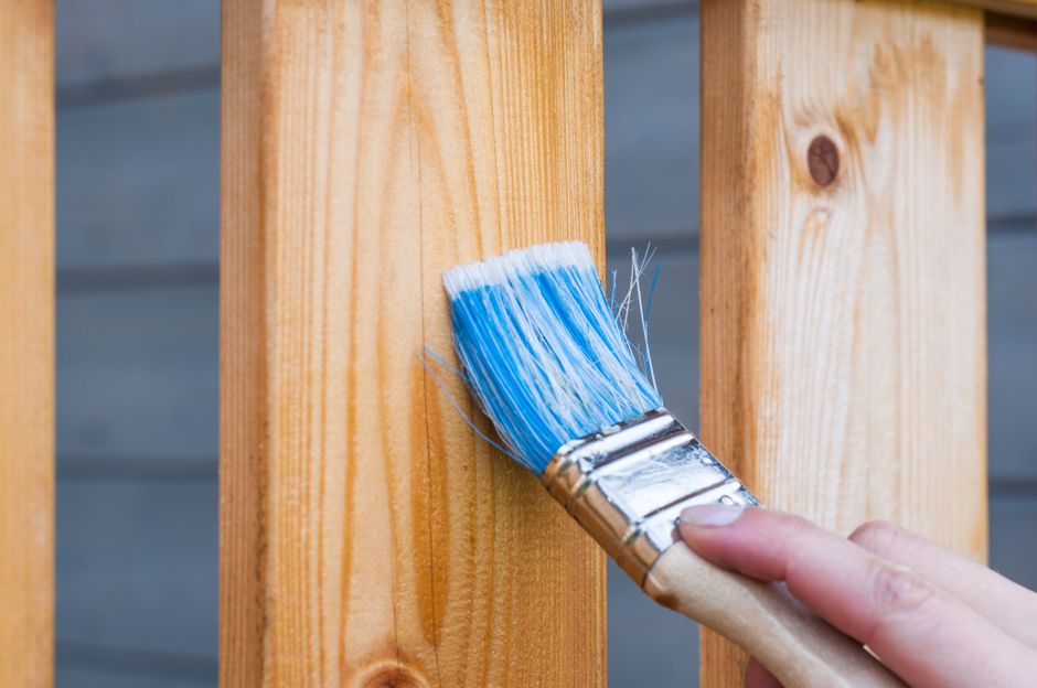 A hand painting a wooden board with a blue paintbrush